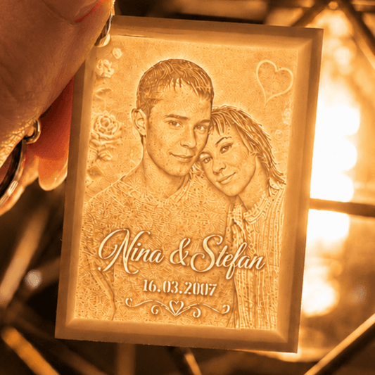 Kleiner personalisierter Lithophane-Schlüsselanhänger mit Paarfoto und Namen, in der Hand gehalten vor warm leuchtender Lampe zoom
