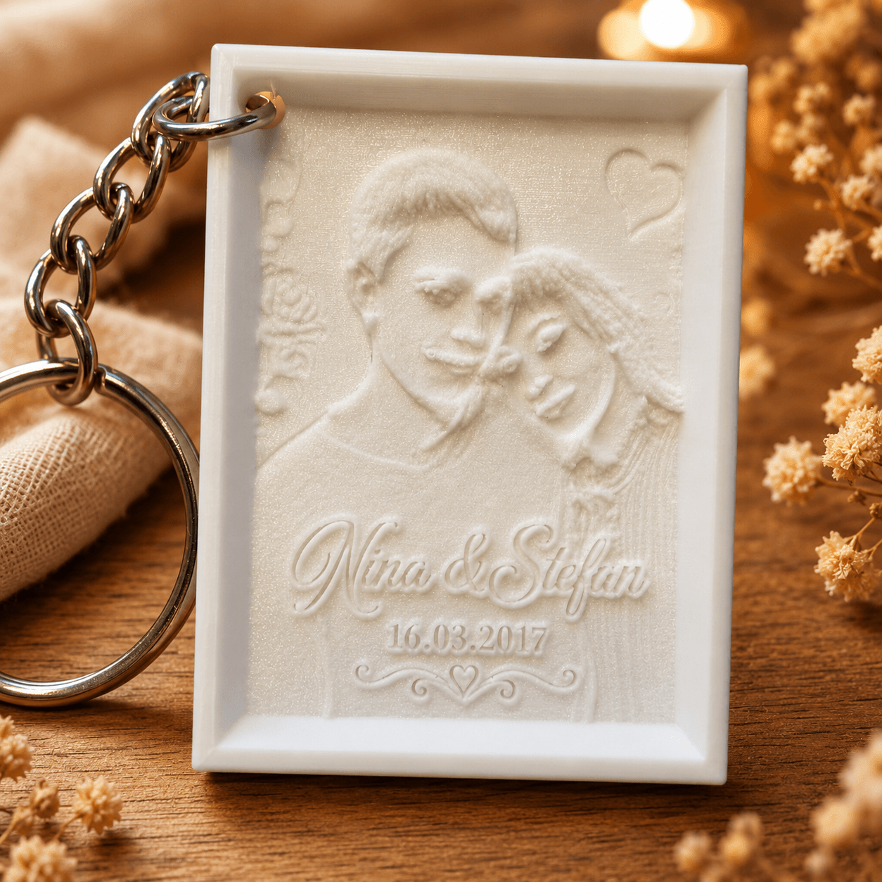 Personalisierter Lithophane-Schlüsselanhänger mit Paarfoto, Namen und Datum auf warmem Holzhintergrund mit dekorativen Trockenblumen
