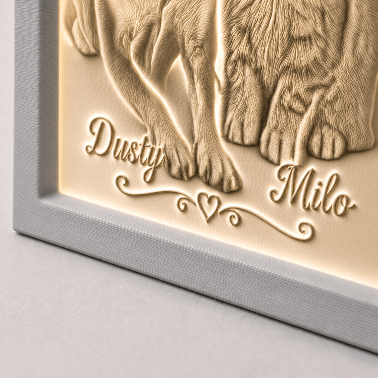 Detailaufnahme der personalisierten Gravur Dusty und Milo mit Herzornament auf warmweiß leuchtendem 3D-Lithophane im grauen PLA-Rahmen